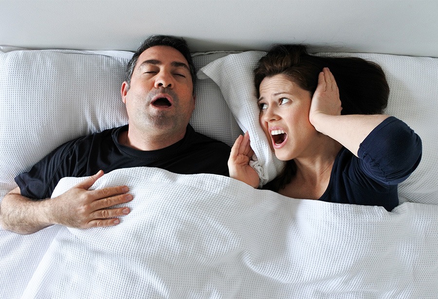 Woman covering her ears in bed next to snoring man in need of NightLase snoring treatment