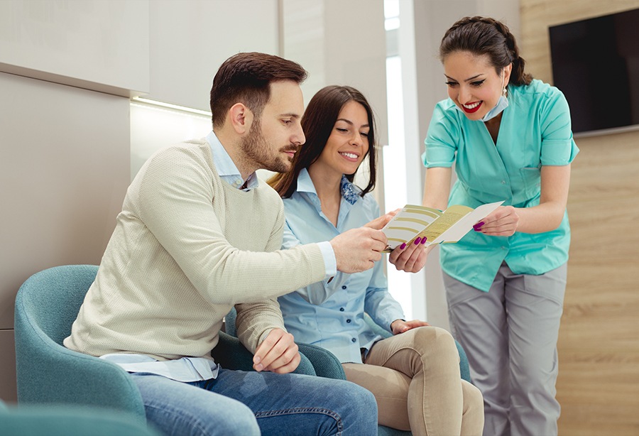 Dental team member giving two dentistry patients dental insurance information