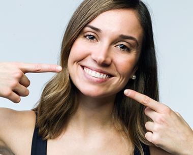 Woman pointing to smile after laser assisted conservative dentistry