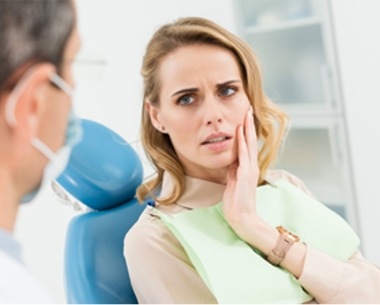 Woman in dental chair for emergency dentistry holding cheek in pain