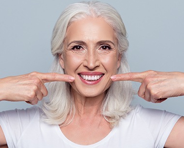 Woman pointing to her smile after dental implant tooth replacement