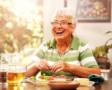 smiling woman with dental implant supported denture eating a meal
