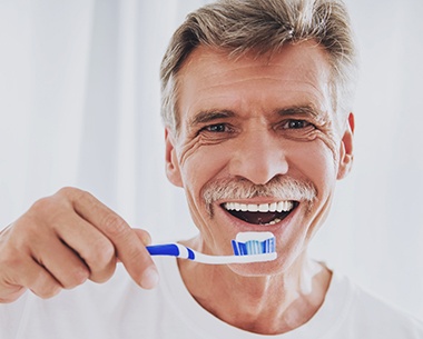 Man brushing teeth to maintain dental implant retained dentures