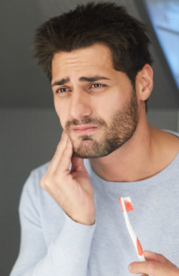 Man holding toothbrush while touching his cheek in pain
