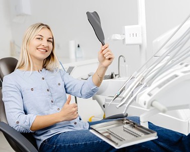 Cosmetic dentistry patient holding mirror and making thumbs up gesture