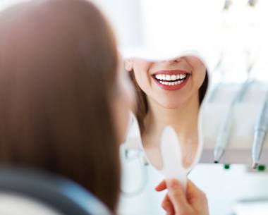 Woman looking at smile in mirror after cosmetic dentistry