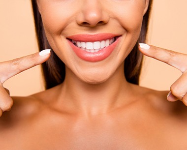 Woman pointing to smile after porcelain veneer treatment