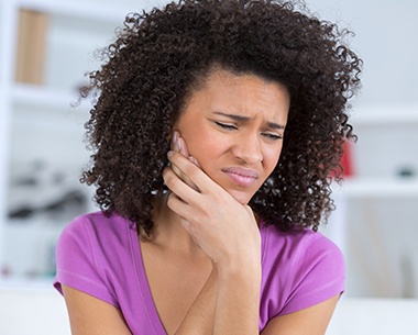 Woman in need of a wisdom tooth extraction holding her jaw