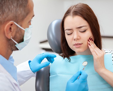 Young woman in dental chair holding cheek in pain before wisdom tooth extraction