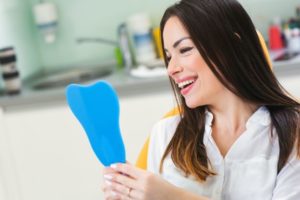 Happy patient using mirror to admire the results of her dental bonding