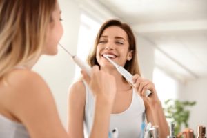 Young woman in front of mirror, using electric toothbrush to clean her teeth