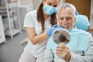 Male patient using mirror to admire his smile after receiving dental implants