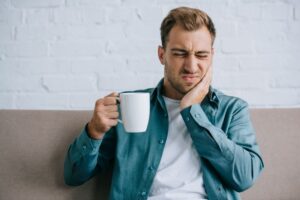 Man holding a cup, dealing with toothache pain