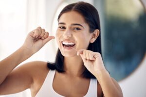 Smiling young woman flossing between her teeth